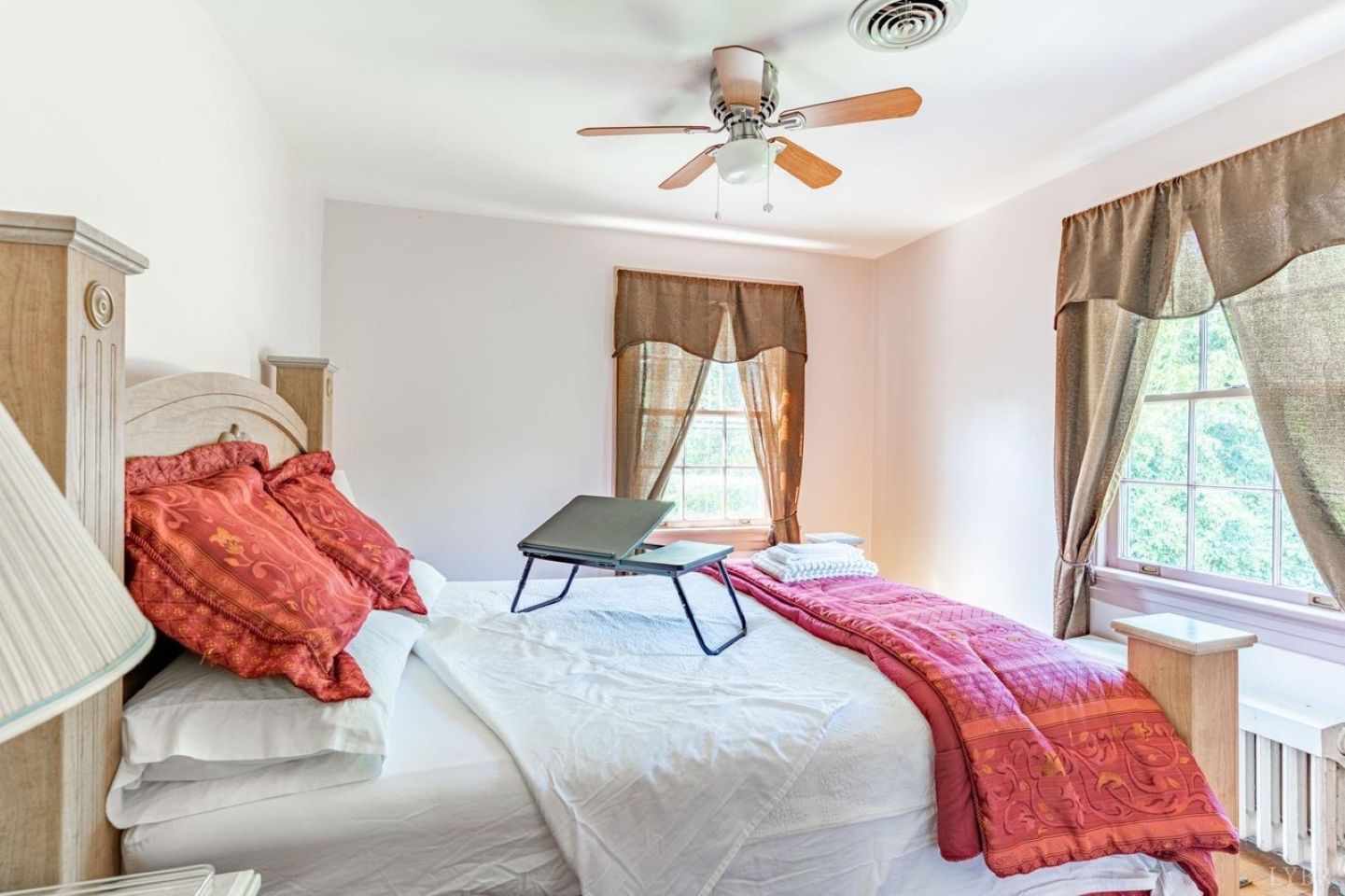 A bedroom with a bed, a laptop on the bed, a ceiling fan, and a window with curtains.