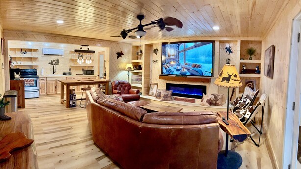 A cozy living room with a large brown leather sofa, a wooden dining table, a television, and a fireplace. - NEW BRAUNFELS - DEER HAVEN CABIN 
 (New Braunfels)