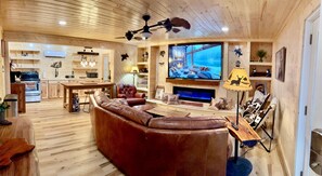 A cozy living room with a large brown leather sofa, a wooden dining table, a television, and a fireplace. - NEW BRAUNFELS - DEER HAVEN CABIN 
 (New Braunfels)