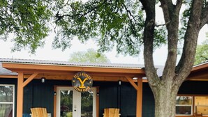 An outdoor seating area with wooden chairs and a table, a covered porch with a sign, and a large tree. - NEW BRAUNFELS - DEER HAVEN CABIN 
 (New Braunfels)