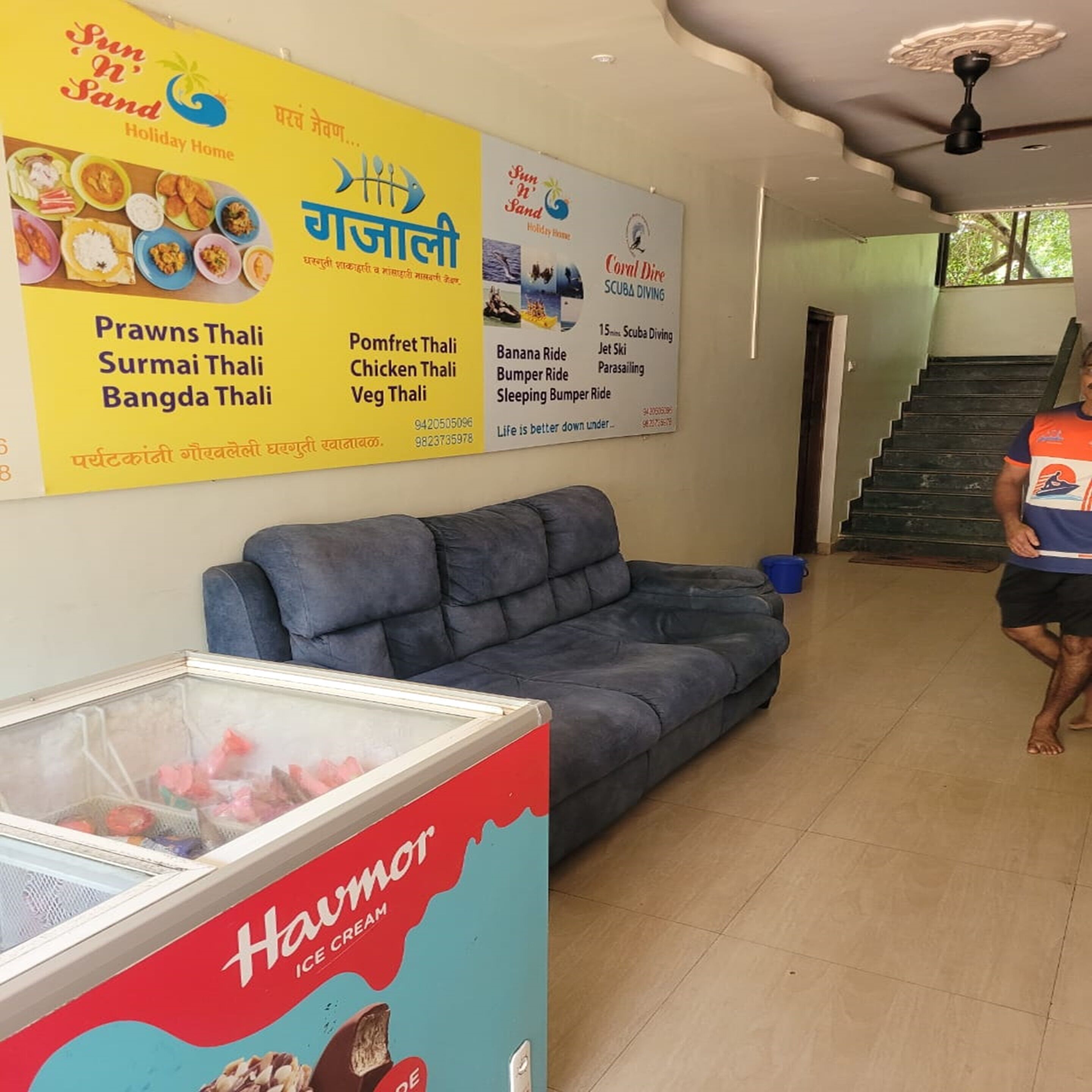 A hotel lobby with a large menu board advertising various dishes and activities, a blue sofa, and an ice cream freezer.