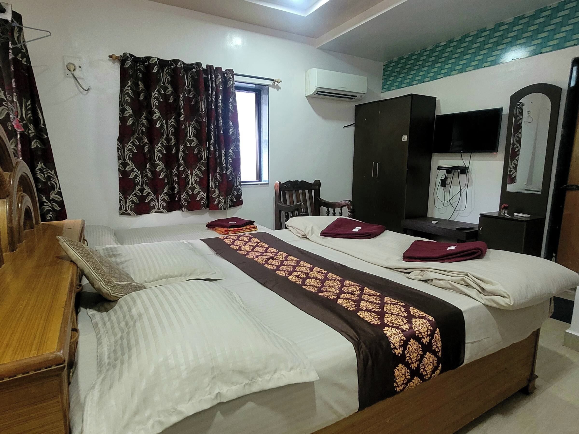 A bedroom with two beds, a wardrobe, a TV, and a window with curtains.
