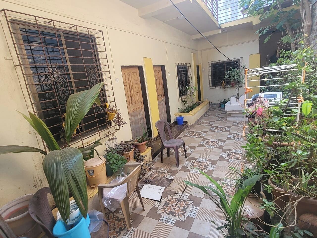 A covered outdoor area with tiled flooring, potted plants, and a chair.