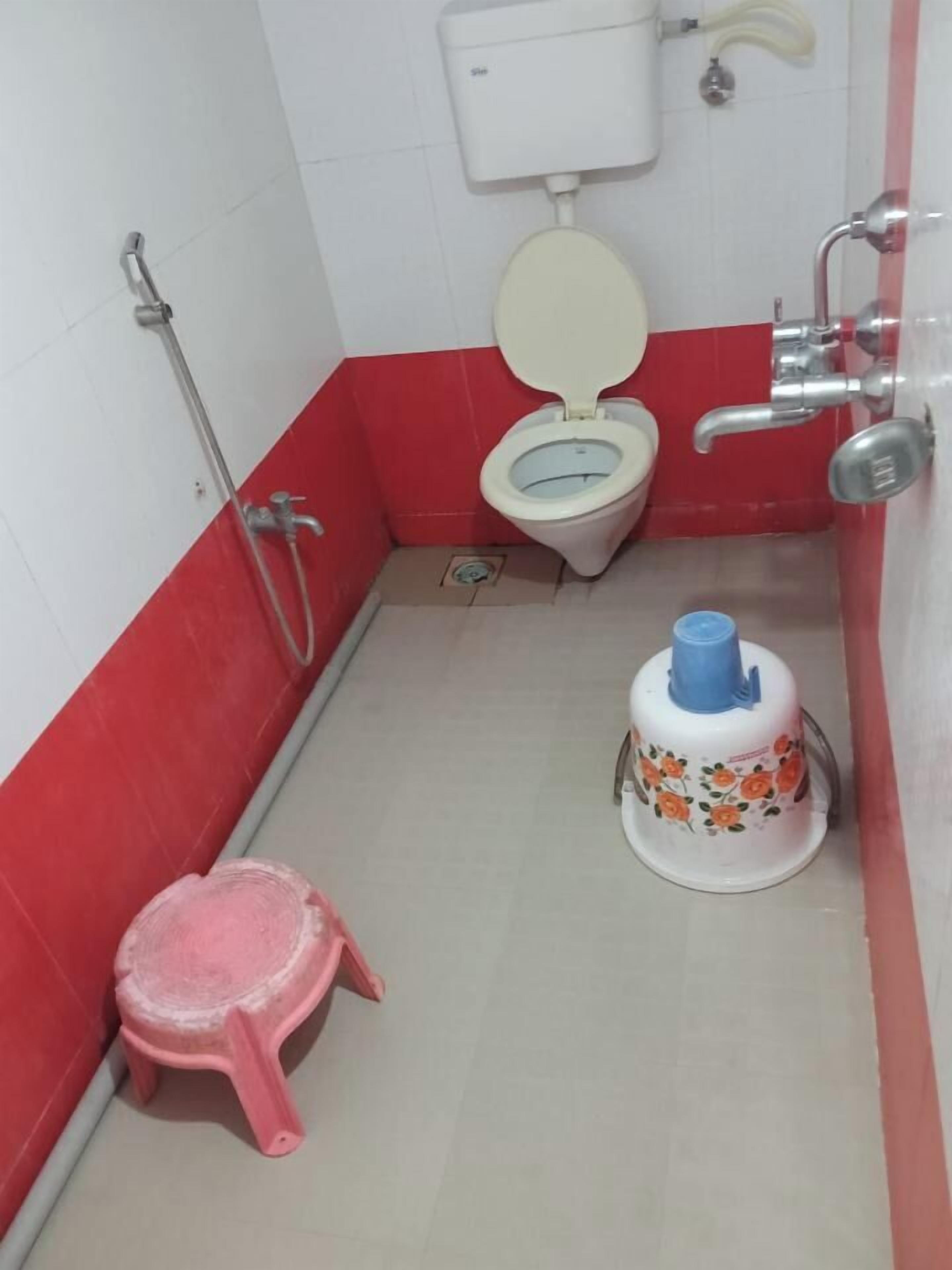 A small bathroom with a toilet, a pink stool, and a water dispenser.