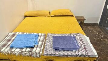 A bed with a yellow bedspread, two pillows, and two folded towels on a checkered and patterned blanket.