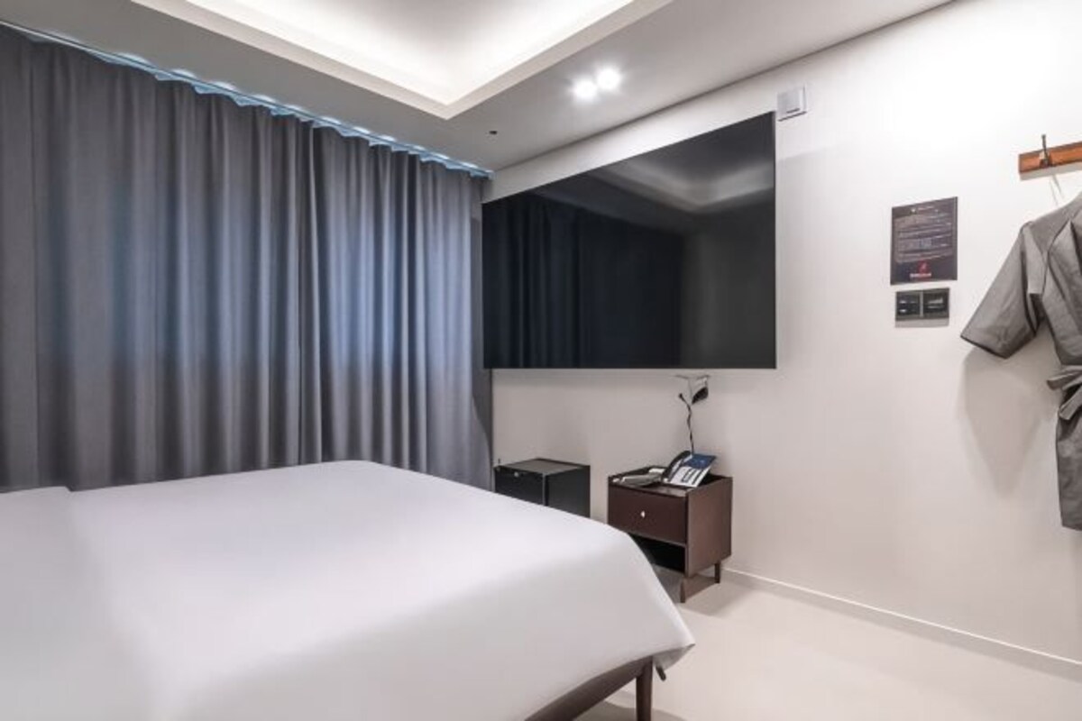 Een moderne hotelkamer met een groot bed, een flatscreen televisie aan de muur, een klein nachtkastje en een jas hangend aan de muur.