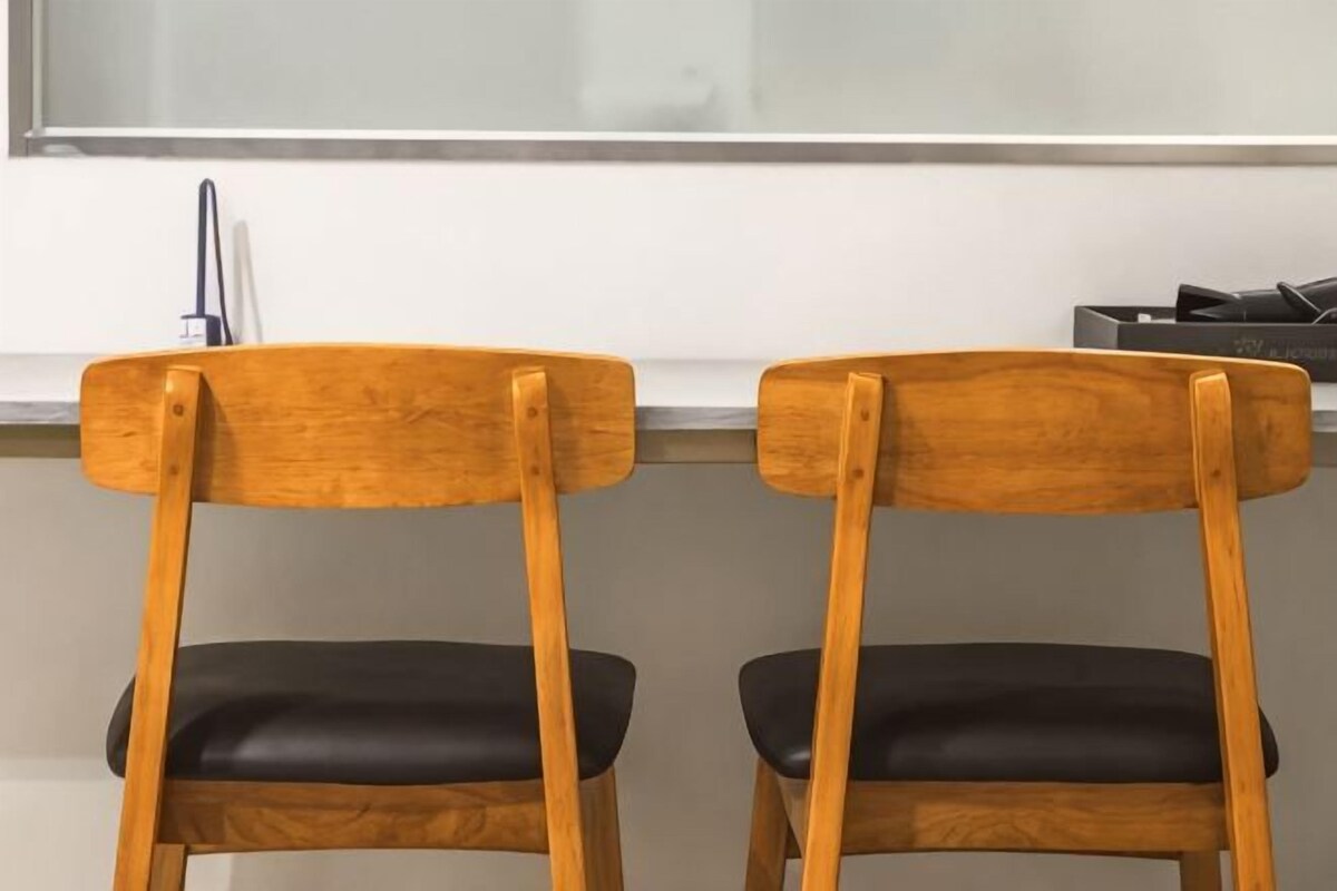 Two wooden chairs with black cushions, positioned at a table with a white countertop and a stainless steel sink.