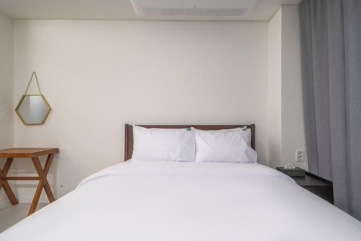 A hotel room with a bed, a bedside table, a lamp, and a window with curtains.