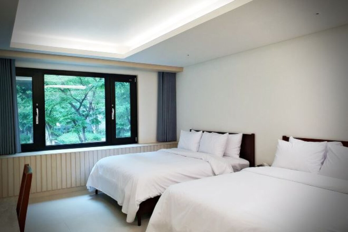 Een hotelkamer met twee bedden, een groot raam en uitzicht op bomen.
