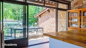 A modern kitchen with large windows, a stone wall, and a wooden bookshelf.