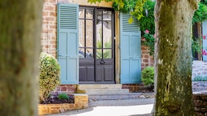 A brick building with a dark door, light blue shutters, and a small garden area in front.