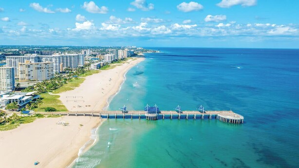 A coastal cityscape with a beach, a pier extending into the ocean, and high-rise buildings in the background. - Pelican Studio w/ Private Patio • Pompano (Pompano Beach)