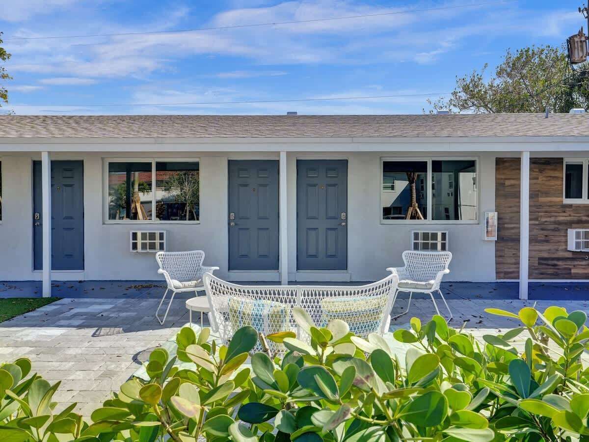 A motel with a row of doors, a covered patio with white chairs, and a wooden wall panel.