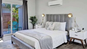 Une chambre moderne avec un grand lit, une table de chevet avec une lampe, une commode et un appareil de climatisation fixé au mur.