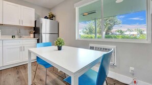 A modern kitchen with white cabinets, a stainless steel refrigerator, and a dining table with blue chairs.