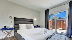 A bedroom with a bed, bedside tables, a desk, a chair, and a view of the outside.