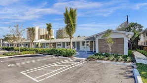 A hotel with a parking lot, modern buildings, and palm trees.