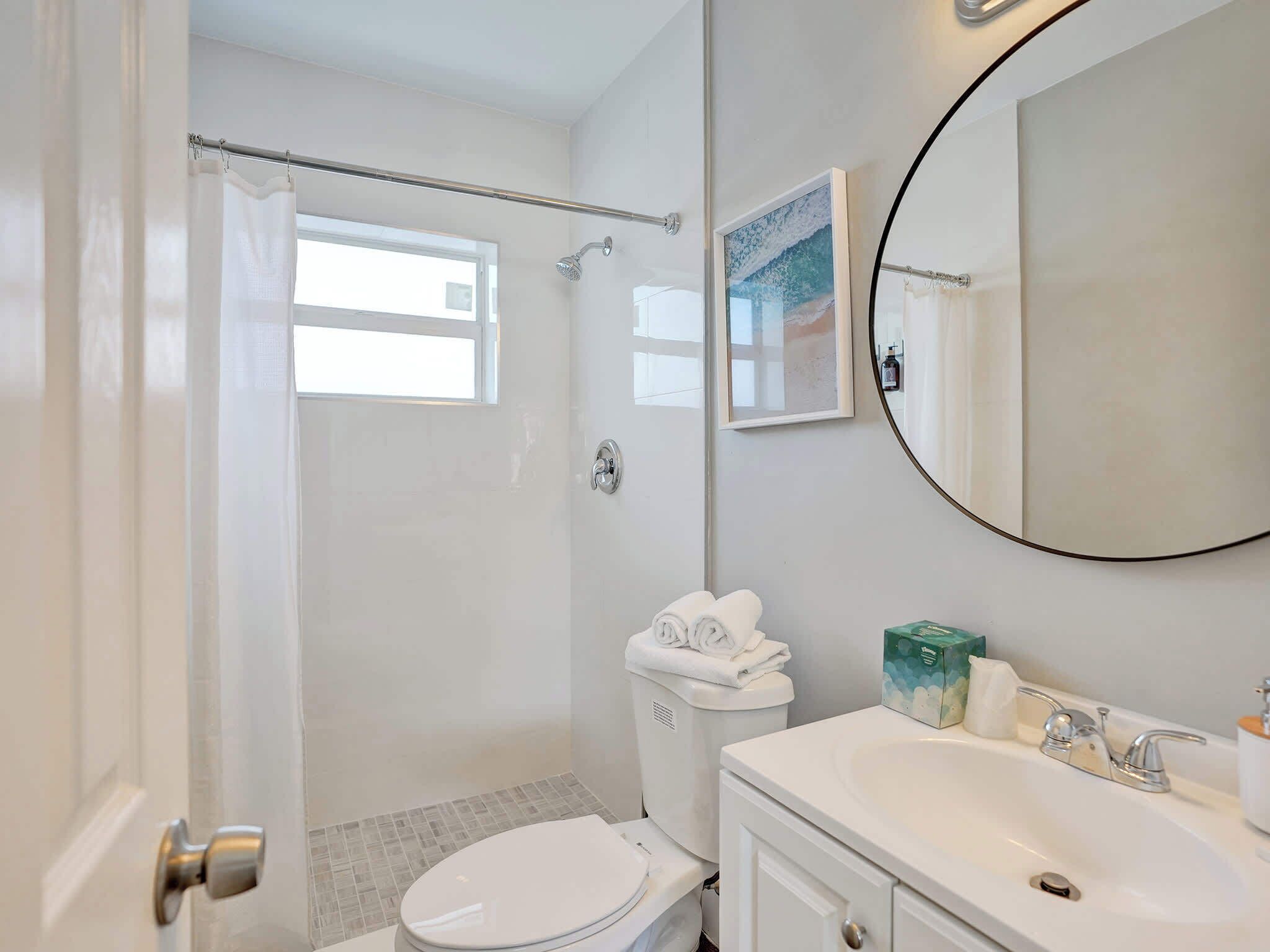 Une salle de bain comprenant des toilettes, un lavabo, un miroir, un rideau de douche et un tableau encadré accroché au mur.