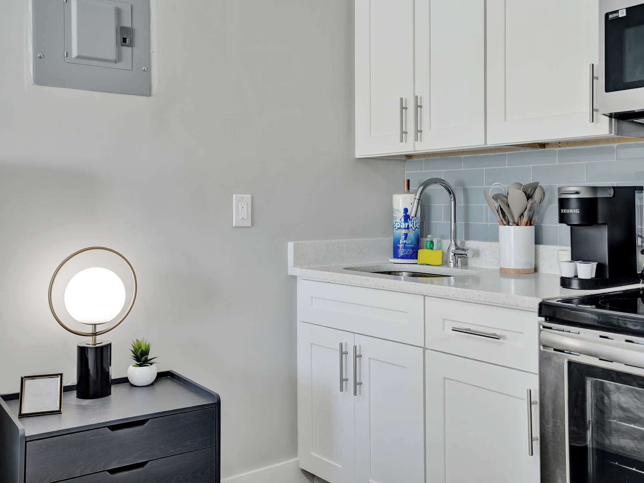 A modern kitchen with white cabinets, a stainless steel range hood, a built-in microwave, and a coffee maker.