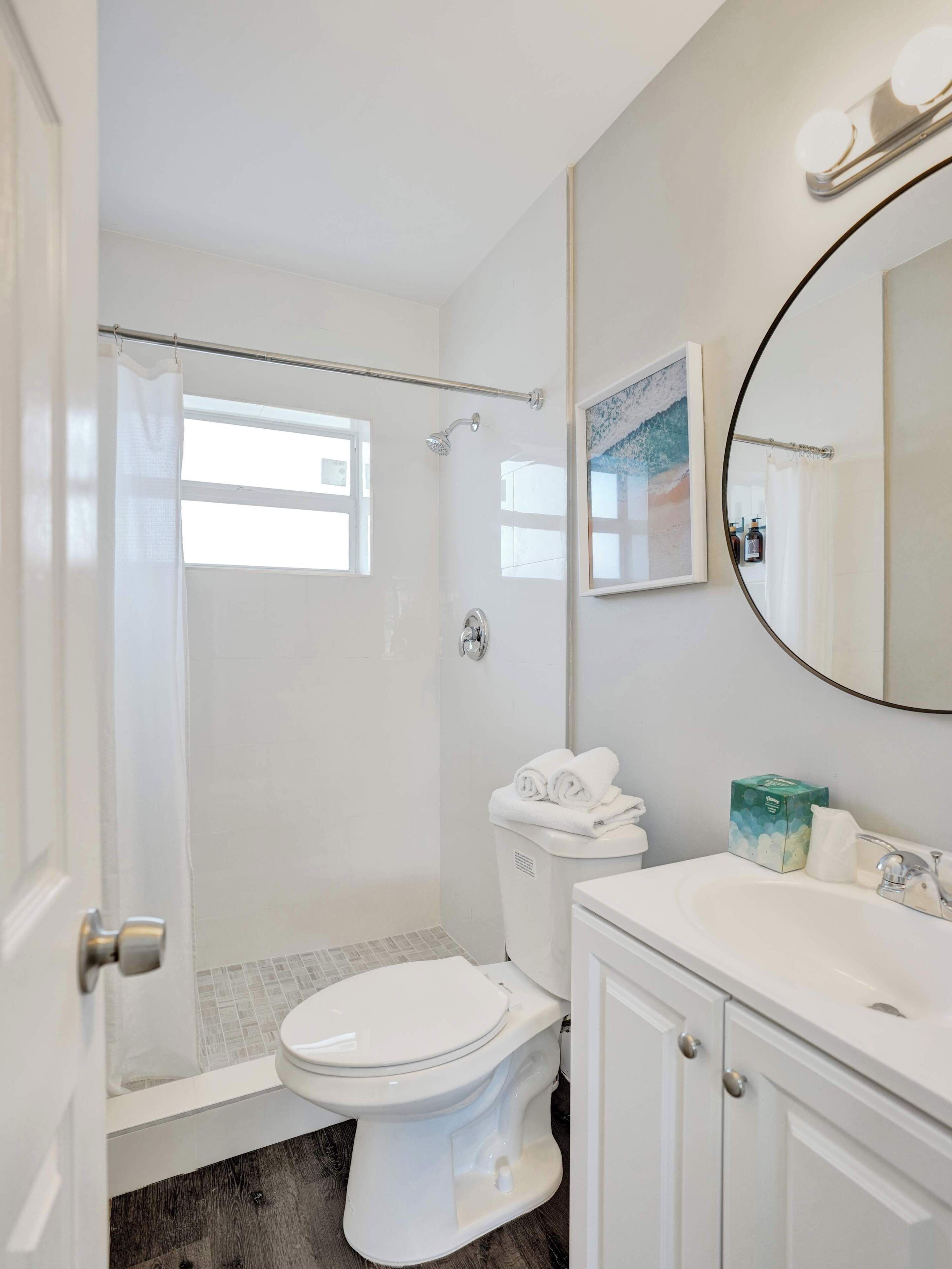 A bathroom with a shower, toilet, sink, and a mirror.
