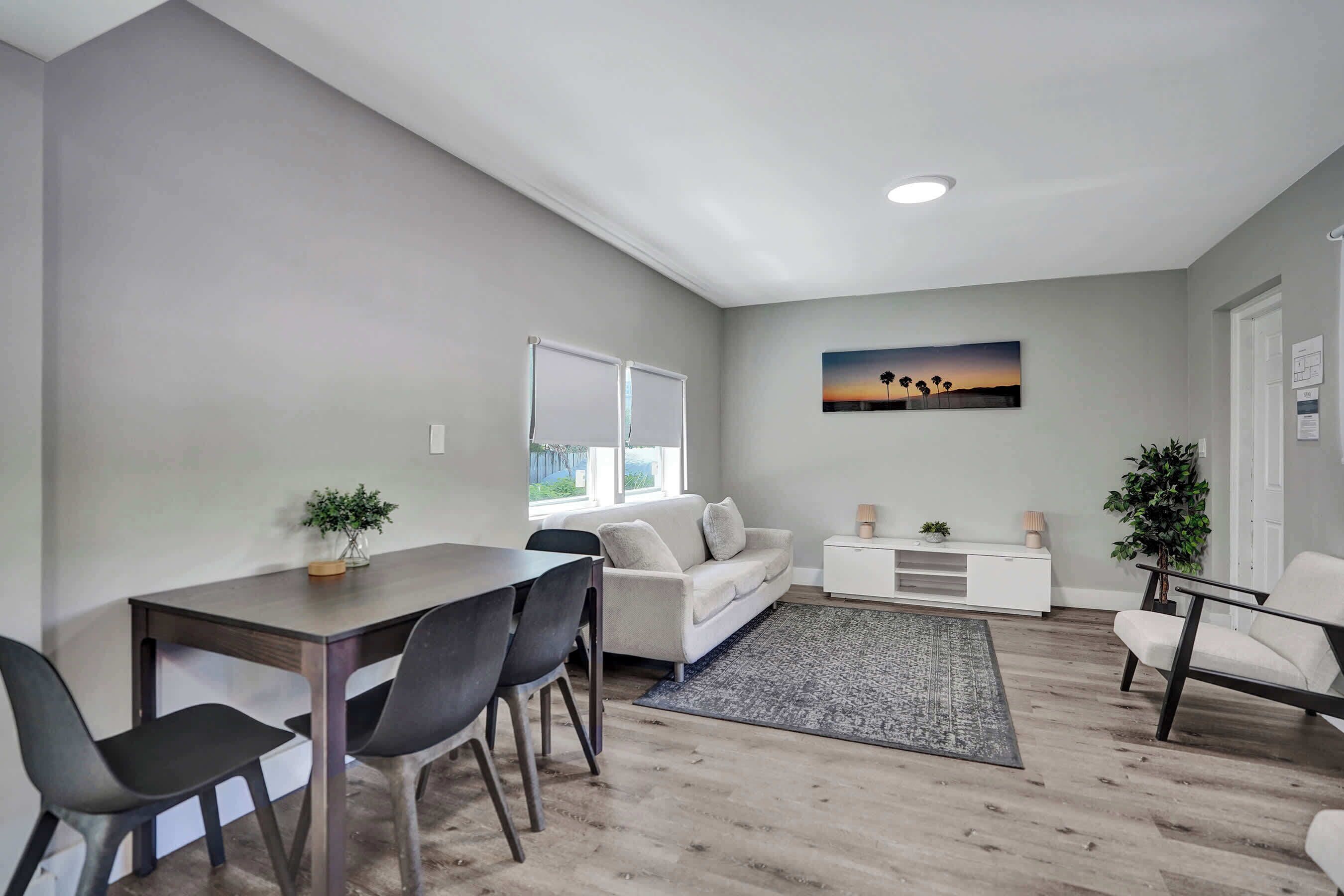A modern living room with a dining area, a white sofa, a coffee table, and a painting on the wall.