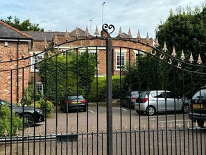 A gated entrance with a wrought iron gate and a brick building in the background. - Blackfriars House, overlooking Chester Racecourse (Chester)