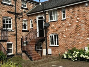 A brick building with a black staircase, a satellite dish, and a small garden with white flowers. - Blackfriars House, overlooking Chester Racecourse (Chester)