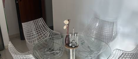 A modern glass table with four chairs, a vase with flowers, and a door with the number 142.
