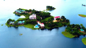 An aerial view of a small island with multiple buildings, including a large pink house and several smaller structures with colorful roofs, surrounded by water.