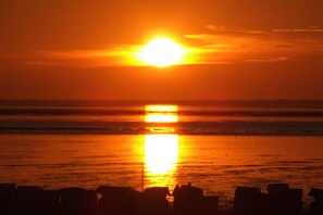 A sunset over a calm sea with a silhouette of a coastal structure in the foreground.
