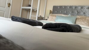 En pænt redt seng med foldede håndklæder, en grå polstret sengegavl og et hvidt skab i baggrunden.