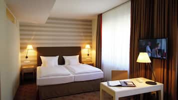 Habitació d'hotel amb un llit de matrimoni, dues làmpades de nit, un televisor penjat a la paret, una taula de nit amb una làmpada i una catifes amb disseny.