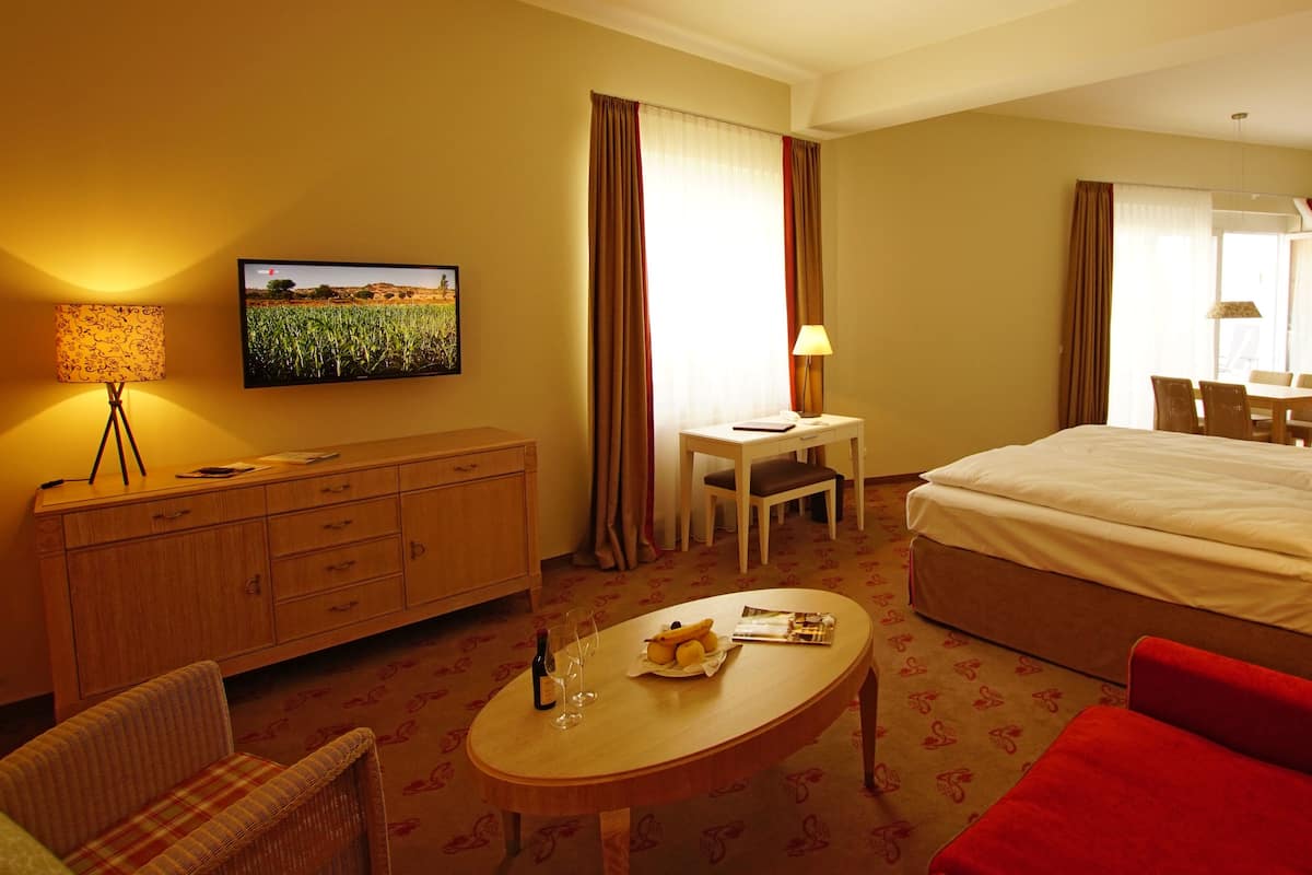 A hotel room with a bed, a desk, a television, a dining table, and a red sofa.
