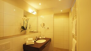 A modern bathroom with a large mirror, a sink, and a shower area. - Landhotel Sanct Peter (Bad Neuenahr-Ahrweiler)