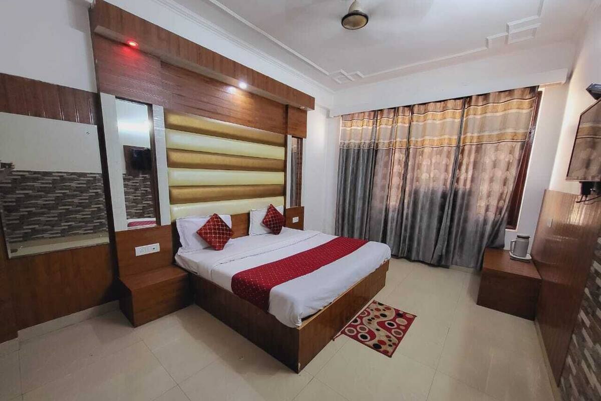 A bedroom with a wooden headboard, a bed with red bedding, a bedside table, and a window with curtains.