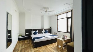 A modern bedroom with a large bed, a bedside table, a small table, and a window. - Hotel New Blue Sapphire Katra (Reasi)