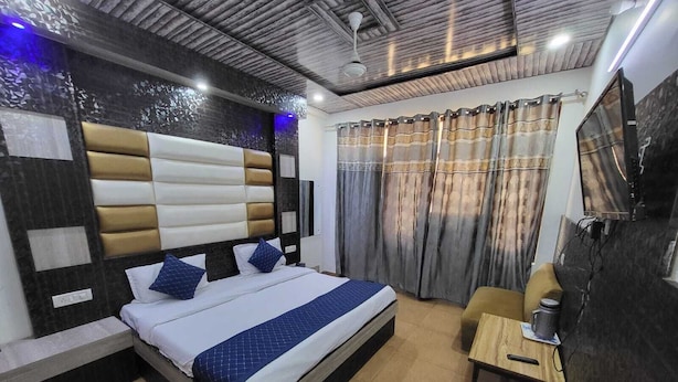 A modern bedroom with a large bed, a small table, a chair, and a TV. - Hotel New Blue Sapphire Katra (Reasi)