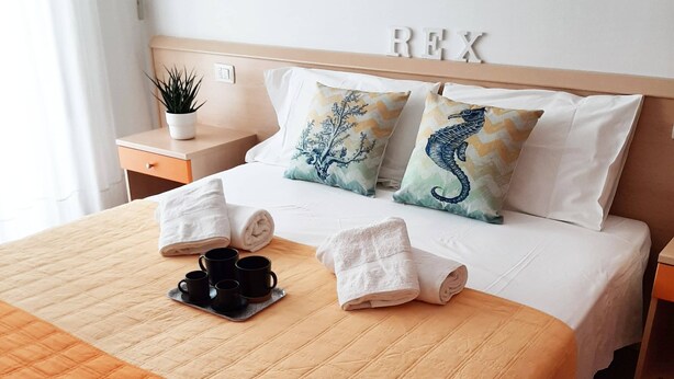 A neatly made bed with a quilted orange blanket, two pillows with seahorse designs, and a bedside table with a plant and a mug. - Residence Rex (Chioggia)