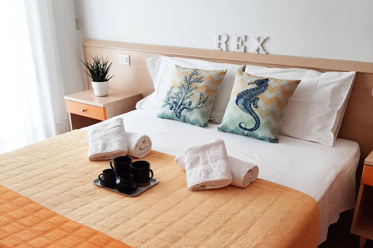 Una cama bien hecha con un edredón naranja acolchado, dos almohadas con diseño de caballitos de mar y una mesita de noche con una planta y una taza.