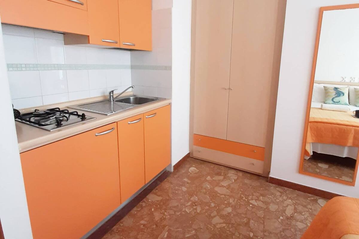 Una cocina compacta con gabinetes color naranja, un lavamanos y una estufa a gas.