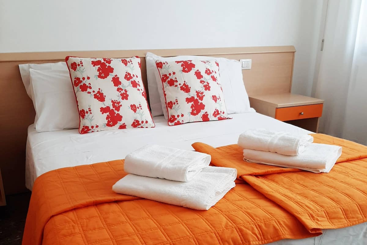 Una cama bien hecha con un edredón naranja, almohadas blancas y toallas blancas dobladas.
