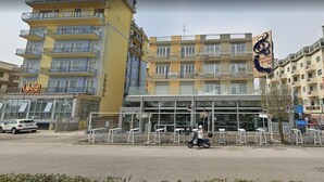 A multi-story building with a cafe on the ground floor, a glass entrance, and a parking area. - Residence Rex (Chioggia)