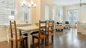 A spacious dining area with a wooden table and chairs, a chandelier, and large windows with blinds. - Emerald Gem by AvantStay | Pool Access, 3mins to Beach! (Watersound)