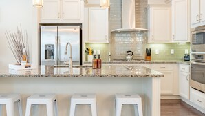 A modern kitchen with white cabinets, a stainless steel refrigerator, a built-in oven, and a granite countertop. - Emerald Gem by AvantStay | Pool Access, 3mins to Beach! (Watersound)