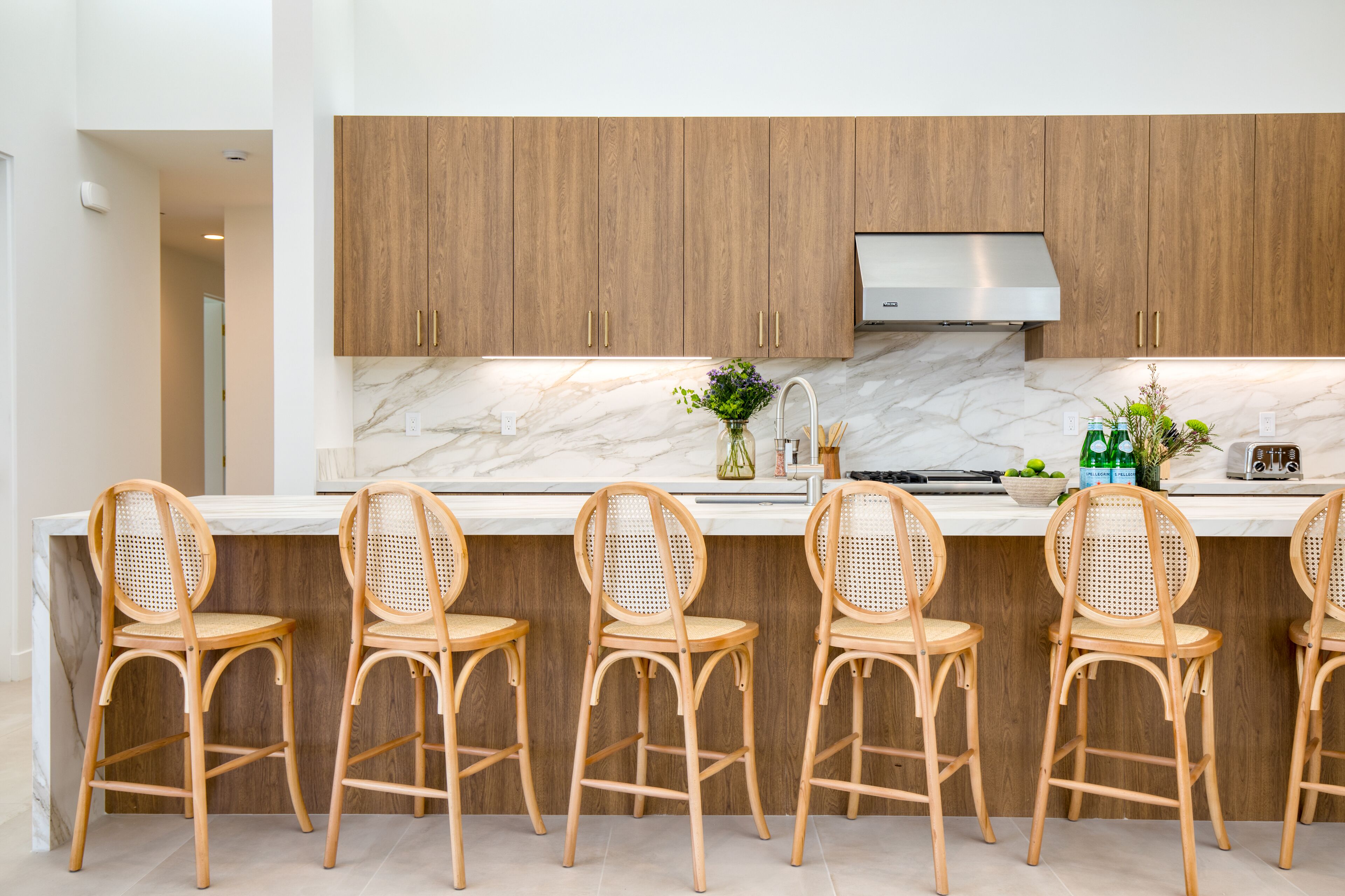 A modern kitchen with wooden cabinets, a marble countertop, and four wicker chairs.