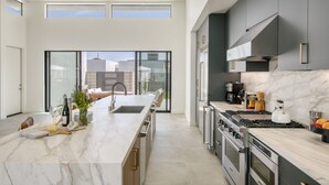 A modern kitchen with a marble countertop, stainless steel appliances, and a large window overlooking the city.