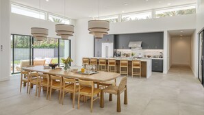 A spacious kitchen with a central island, wooden chairs, and pendant lighting.