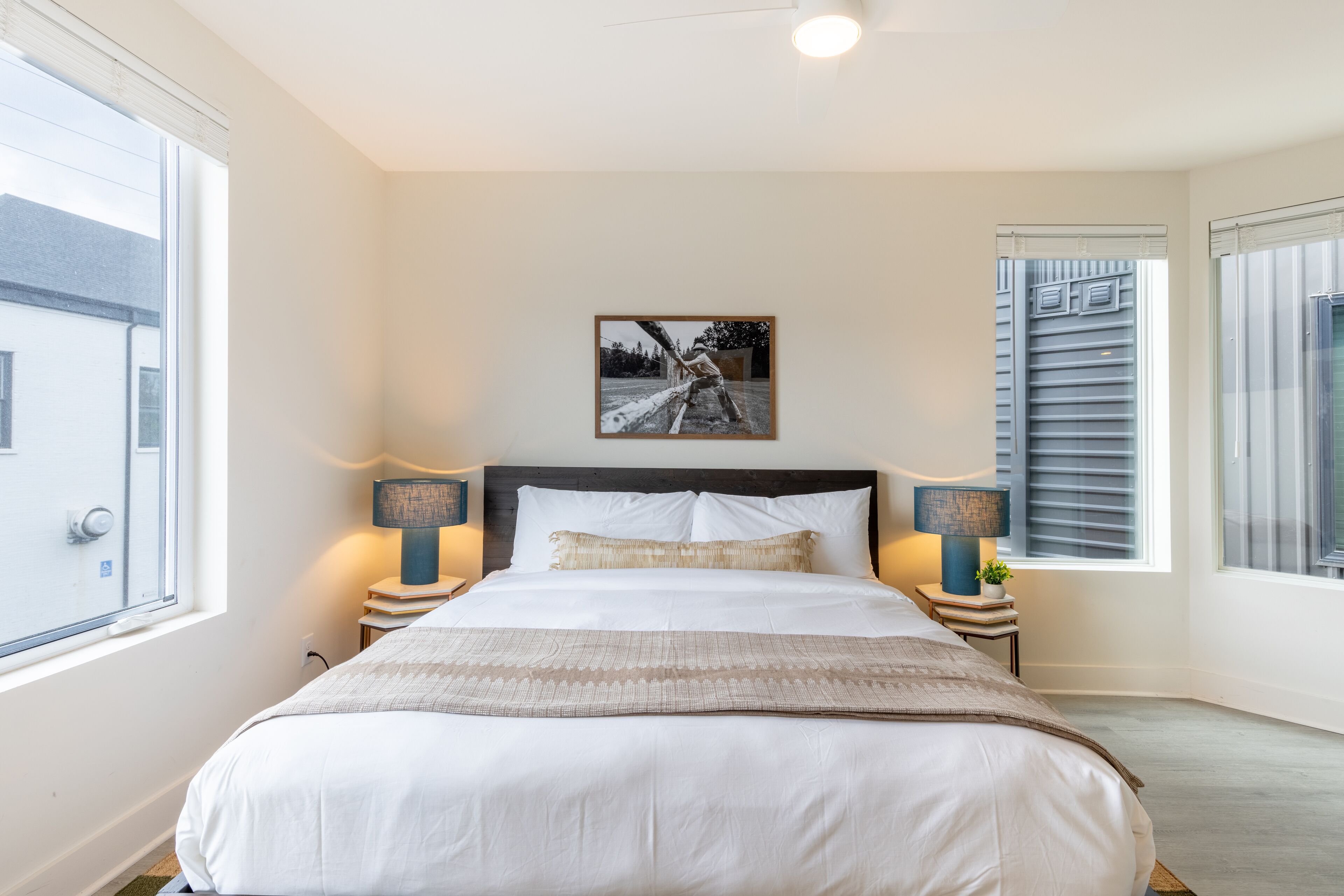 A neatly made bed with white linens, two bedside lamps, and a framed picture above it.