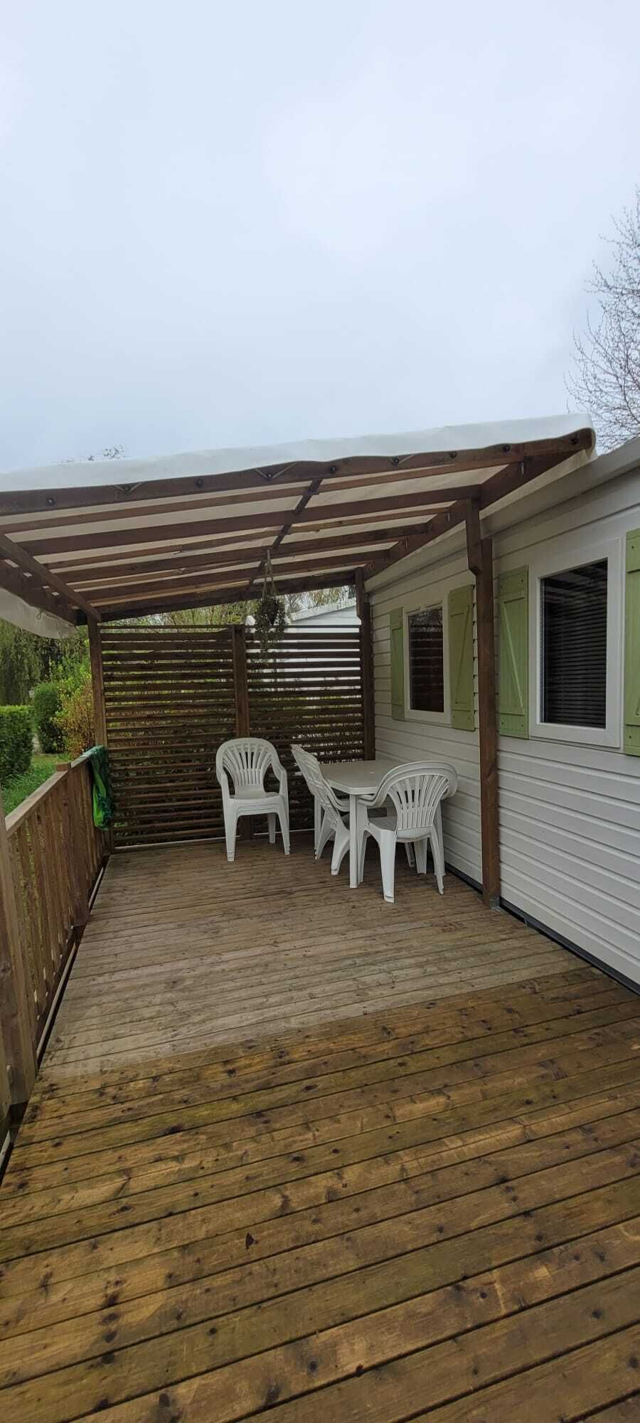 A wooden deck with a pergola, white plastic chairs, and a table.