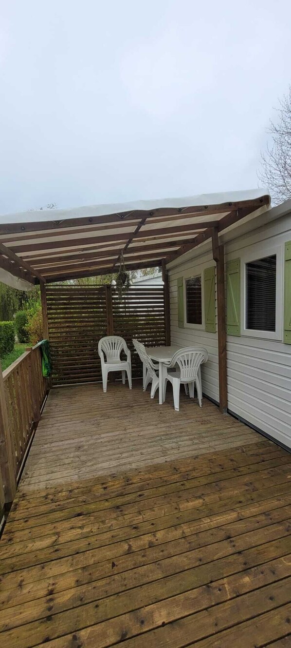 A wooden deck with a pergola, white plastic chairs, and a table.